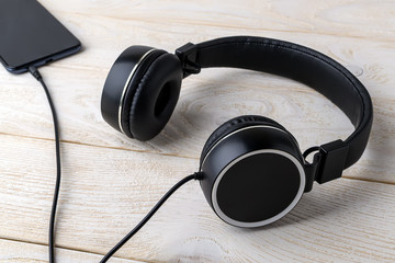 Black headphones connected to a smartphone on a wooden table. Listen to music. Modern personal device with touchscreen for music and communication.
