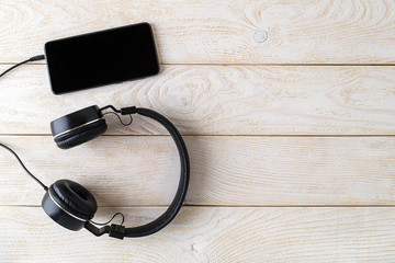 Black headphones connected to a smartphone on a wooden surface. Listen to music. Modern personal device with touchscreen for music and communication.