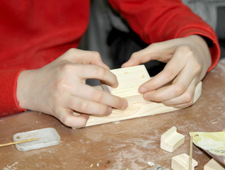 Fototapeta na wymiar The child glues the part to the workpiece. Children 's master class on manufacturing of wooden ship