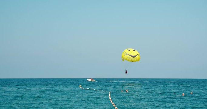 Parasailing at sea for tourists. A man flies on a parachute tied to a motor boat. A smiley is drawn on the parachute as a symbol of the pleasure of relaxing at sea.