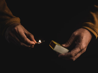 The hands of an adult man holding a burning match on black background