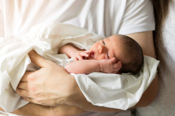 Father holds naked newborn son in his hands in a white diaper.