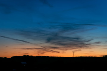 Horizontleuchten in der abenddämmerung von blau zu orange mit Silhouette Strommast und Landschaft