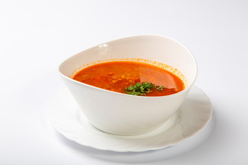Beef goulash soup with tongue. A white oval plate with red soup stands on a white background