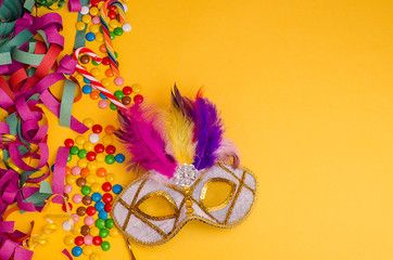 Carnival. Festive background. Carnival mask with feathers on a yellow background with tinsel, ...