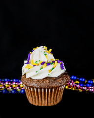 Single miniature cupcake against a black background with strings of colorful beads in the background.