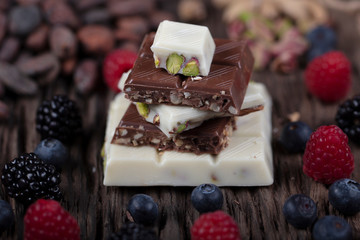 Delicious chocolate cubes, forest fruits on wooden ground. An assortment of white, dark, and milk...