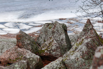The rocky shore of a large lake in early spring, large stones and melting ice near the shore on a cloudy spring day.