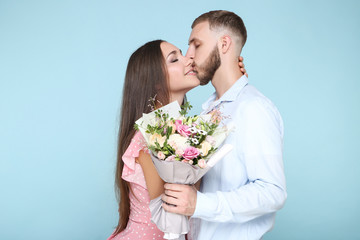 Happy young couple with bouquet of flowers on blue background