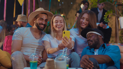 Group portrait of attractive positive friends chilling relaxing using mobile phone device having fun conversation on the party.