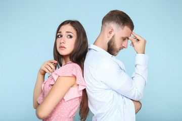 Fototapeta premium Young upset couple standing by the back to each other on blue background