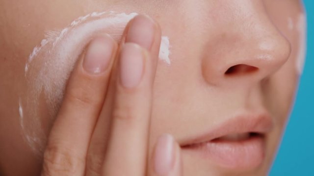 close-up of woman moisturizing and massaging cheek and under eye zone with cream