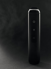 Naklejka premium Electronic dry herb vaporizer on black background and smoke in the background