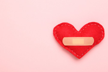 Red fabric heart with bandage on pink background