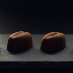 Obraz na płótnie Canvas Two pieces of Coffee bean shape Chocolate on black stone plate