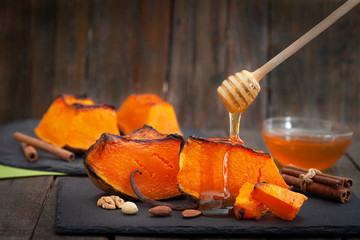 Peaces of baked butternut squash pumpkin with honey and nuts on wooden table. Healthy vegan food.
