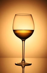 A glass of white wine in the backlight against a bright, yellow-orange background.