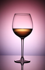 Glass of white wine in the backlight on a bright, lilac-pink background.