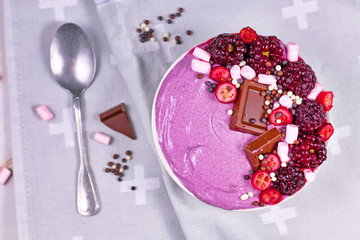 Fruit smoothie bowl decorated with healthy red raspberry, cranberry, small marshmallows and chocolate pieces