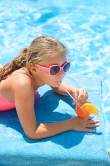 Beautiful little girl with sunglasses relaxing at   swimming pool with coctail and fruit