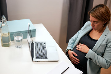 Pregnant businesswoman having stomach ache and touching belly.