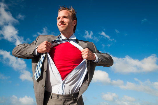 Smiling Businessman Standing Outdoors Pulling His Shirt Apart To Reveal A Bright Red Superhero Costume