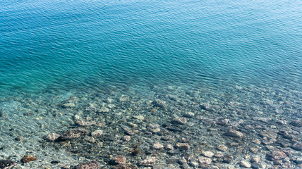 Top up view of multicolored pebble and average size stones at sandy bottom of sea beach under clear water in Norway, close to Sandnessjoen. Sea bottom view through green blue clear water of Atlantics