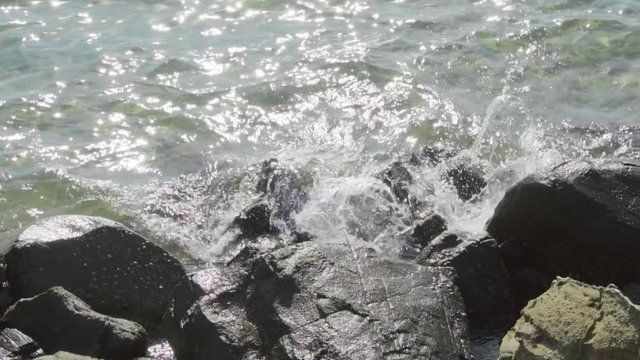 Wave move towards shore and splash on rough stones of breakwater, slow motion shot