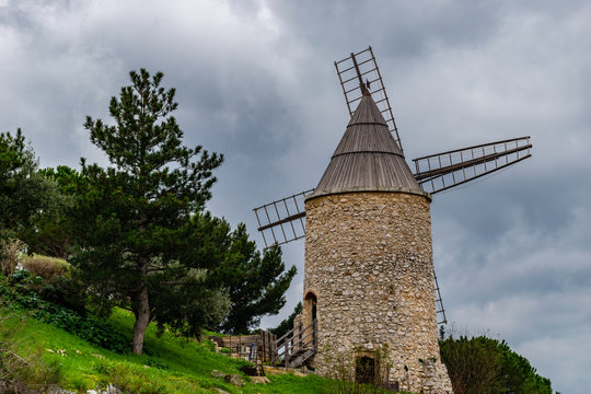 An old stone windmill in a French village on a hill against the background of a cloudy sky