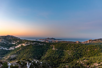 Sunrise at Calanque de Morgiou (Marseille, France): the breathtaking view of the cliff mountain landscape and the island Riou in the distance under the warm soft sunlight