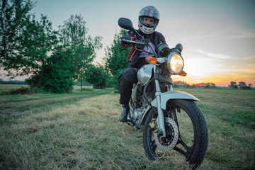 Fototapeta na wymiar young attractive woman on motorcycle on dirt road at sunset