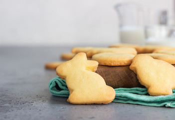 Easter cookies on a wooden cutting board with milk, grey stone background. Homemade butter and sugar cookies. Idea for children snack.