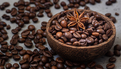 Wooden bowl with roasted coffee beans with star anise, grey stone background.