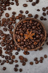 Wooden bowl with roasted coffee beans with star anise, grey stone background.
