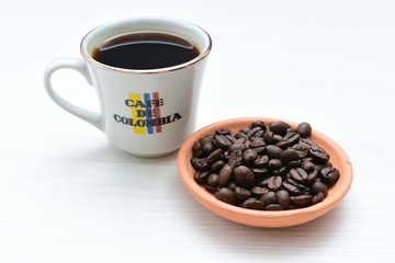 Traditional cup of Colombian coffee with coffee beans on wooden background
