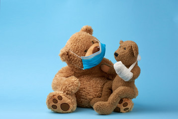 big brown teddy bear sits in a medical mask, in his hands he holds a small toy