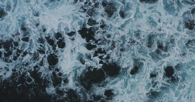 Aerial view of powerful waves breaking over a rocky coastline at dusk, moody nature backgrounds