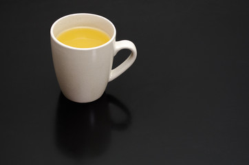 White cup on a black smooth table with reflection, with a yellow tea inside, near a brick wall with copyspace