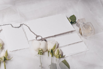 Fototapeta na wymiar Wedding invitation mockup with white roses , papers on white textile background. Top view, flat lay. Wedding stationary. Perfect for presentation of your invitation, menu, greeting cards