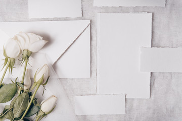 Wedding invitation mockup with white roses , papers on white textile background. Top view, flat lay. Wedding stationary. Perfect for presentation of your invitation, menu, greeting cards