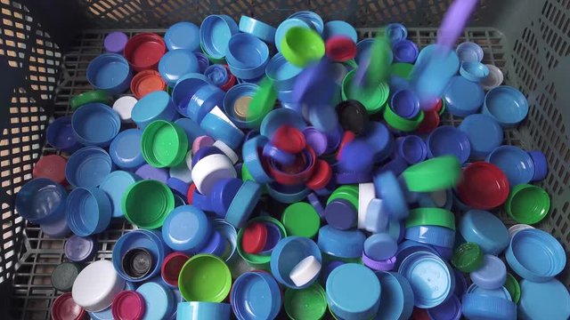 Various size and color plastic bottle caps falling into basket.