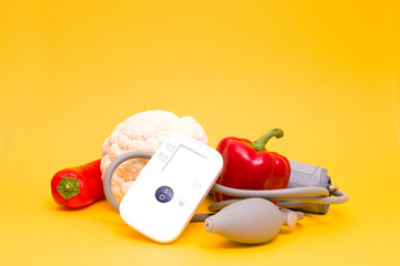 tonometer on a yellow background, vegetables for proper nutrition and dieting, cauliflower and red...