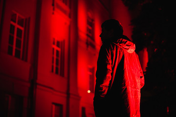 Silhouette of man with hands in pockets standing by building in darkness during night