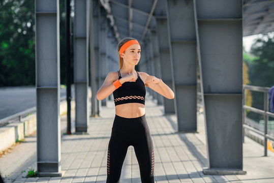 Fitness girl at sportswear makes exercises in the background of sport stadium. Warm up before training. Young sports girl makes stretching.