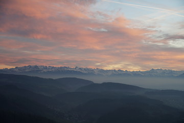 Sunset panorama of Alps over canton Zurich, Switzerland. The whole landscape is veiled in thin fog. The sky is colorful at sunset. 