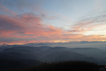 Sunset panorama of Alps over canton Zurich, Switzerland. The whole landscape is veiled in thin fog. The sky is partially colorful at sunset. 