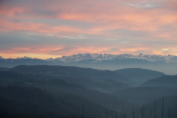 Sunset panorama of Alps over canton Zurich, Switzerland. The whole landscape is veiled in thin fog. The sky covered by various colors at sunset.
