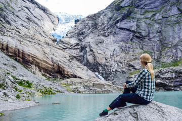 The young woman near the Briksdalsbreen (Briksdal) glacier, which is the sleeve of large Jostedalsbreen glacier. Melting glacier forms the Briksdalsbrevatnet lake with clear water. Norway.