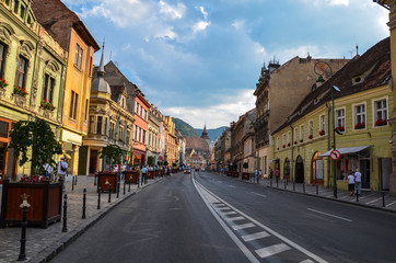 Old street with ancient buildings and stone paved road in Brasov city center, Romania. The Black Church can be seen up above.