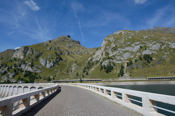Naklejka premium Strada di montagna senza auto su una diga del lago Fedaiacon sfondo delle montagne e del cielo blu 